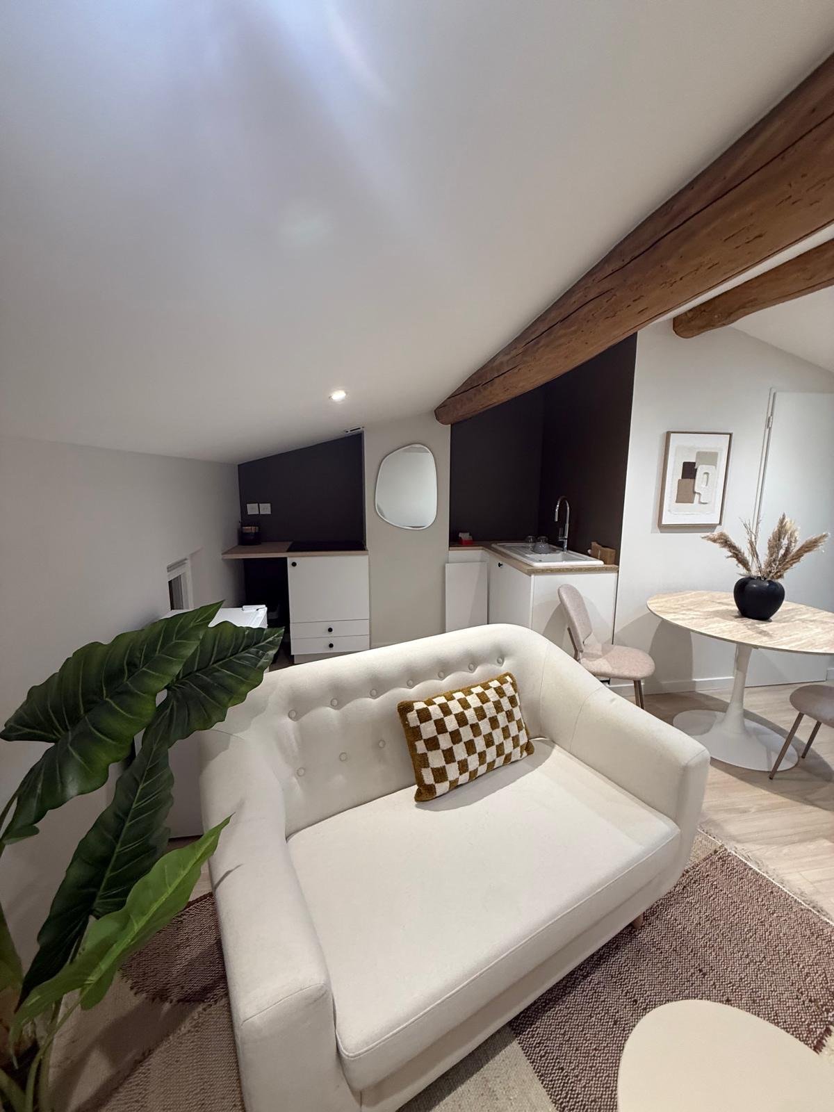 Canapé blanc avec coussin damier doré et kitchenette en arrière-plan